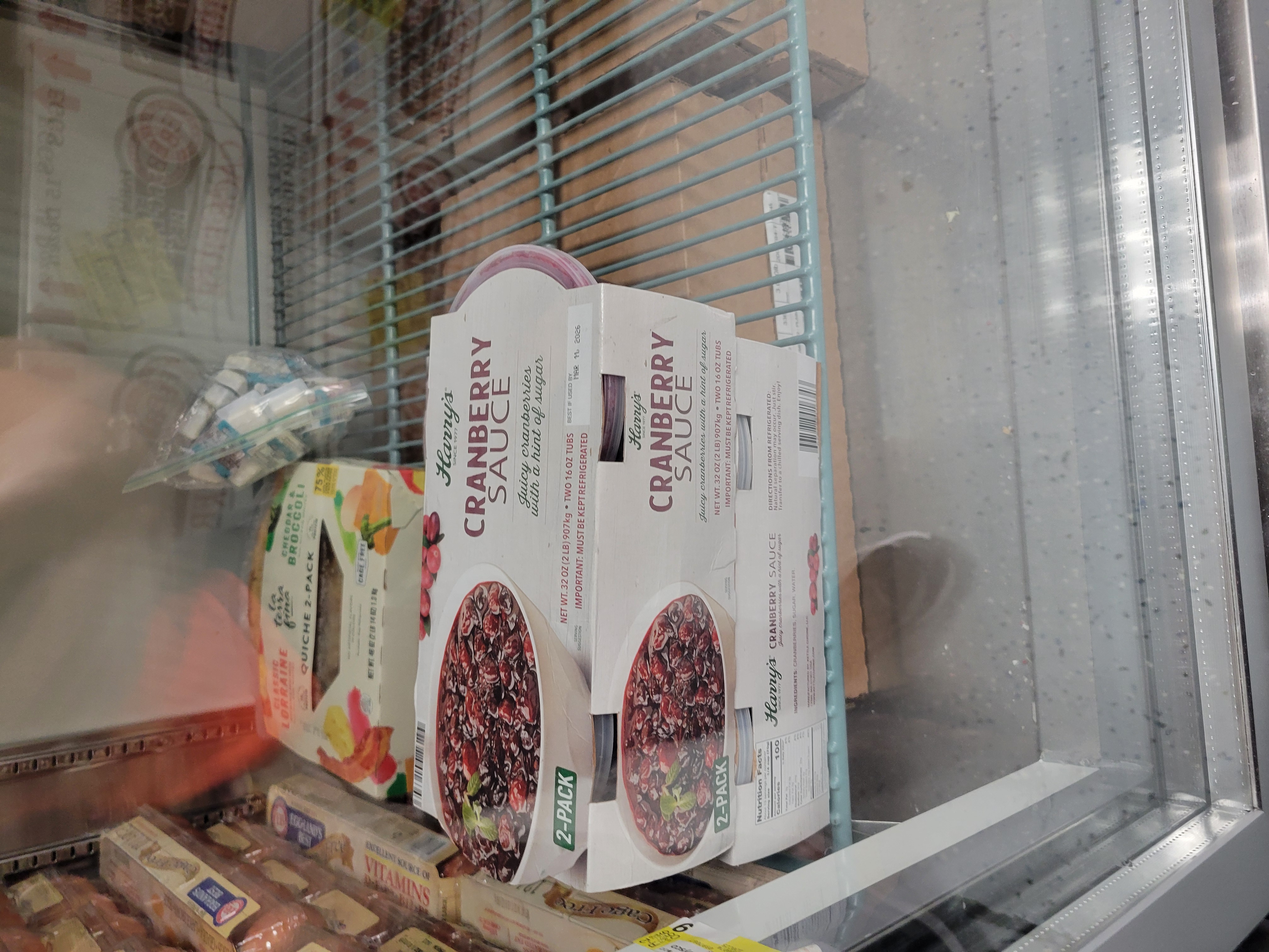 Tubs of cranberries sauce with a pack of quiche on a shelf and cartons of eggs next to it.